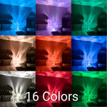 A 3×3 collage of a bedroom scene showing a small LED projector/night light on a bedside table casting water-ripple/aurora-style light across the wall and ceiling. Each panel shows a different color mode (blue, purple, green, warm white, red/orange, etc.). Large text across the bottom center reads “16 Colors.”