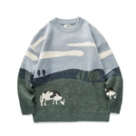 Light blue crewneck knit sweater with a pastoral landscape design—white clouds in the sky above green hills and trees, with small white cows near the hem and on the right sleeve.