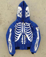 Blue zip-up hoodie laid flat on a concrete surface, featuring bold white skeleton graphics on the chest and arms, plus skull designs on the hood.