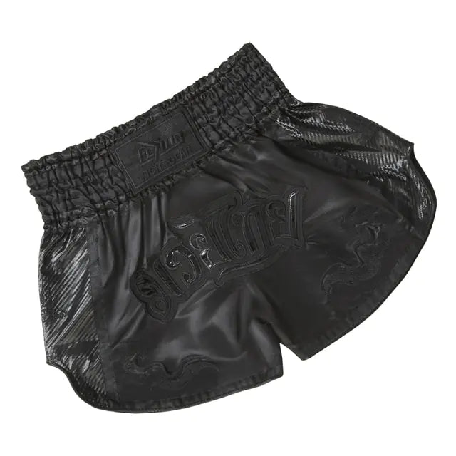 A pair of black satin-style boxing/kickboxing shorts with an elastic waistband, subtle dragon-like detailing, and large raised lettering across the front, shown on a white background.