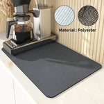 Plain grey rectangular polyester mat placed under a coffee machine on a kitchen worktop, with close-up fabric texture and anti-slip backing details shown.