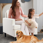 A woman in a pink knit top sits on a white accent chair beside a young girl holding a plush pillow, while a golden retriever lies on the rug in front of them in a bright living room.