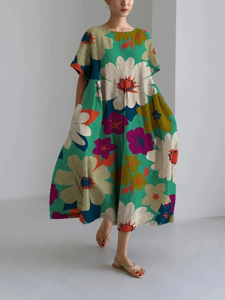 Woman wearing a loose-fitting, white midi dress with short sleeves, featuring bold red-orange floral prints accented with blue centers, paired with flat sandals.