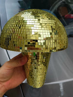 Hand holding a gold mosaic disco-ball style mushroom decoration with mirrored square tiles, shown in front of a car door.
