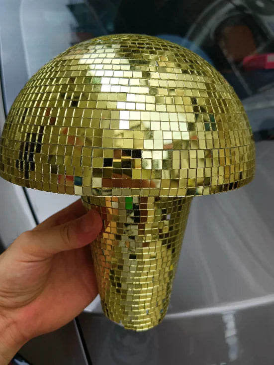 Hand holding a gold mosaic disco-ball style mushroom decoration with mirrored square tiles, shown in front of a car door.