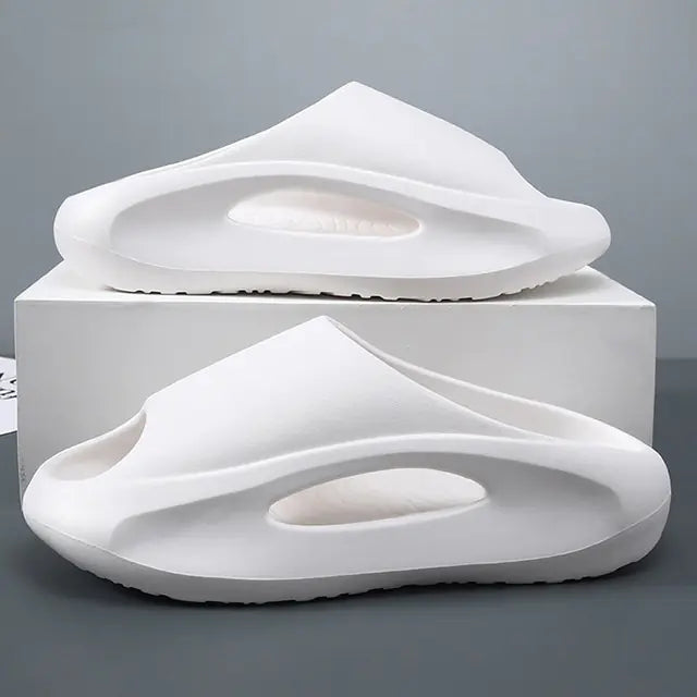 A pair of stylish black slip-on sandals with purple cushioned insoles, featuring cutout designs on the sides and toes, displayed on a white surface next to stacked books.