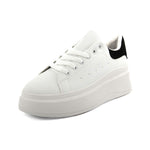 A white platform sneaker with thick soles, white laces, and a black accent on the heel, displayed at an angle against a white background.