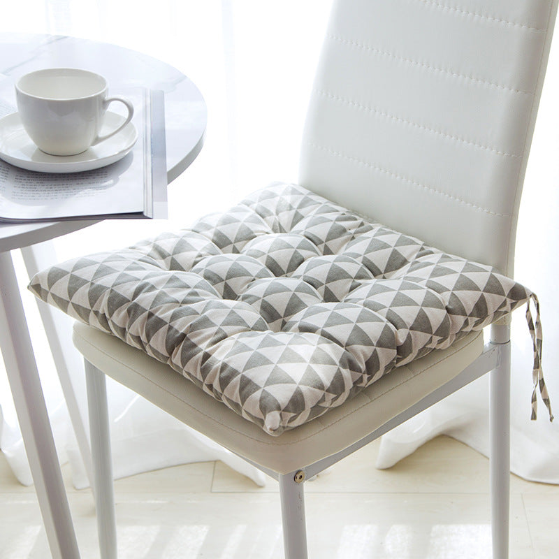 Gray geometric patterned chair cushion on a white chair with a cup and saucer in the background.