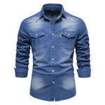Washed blue men’s button-up shirt with a pointed collar, two button-flap chest pockets, light buttons, and rolled cuffs on a white background.
