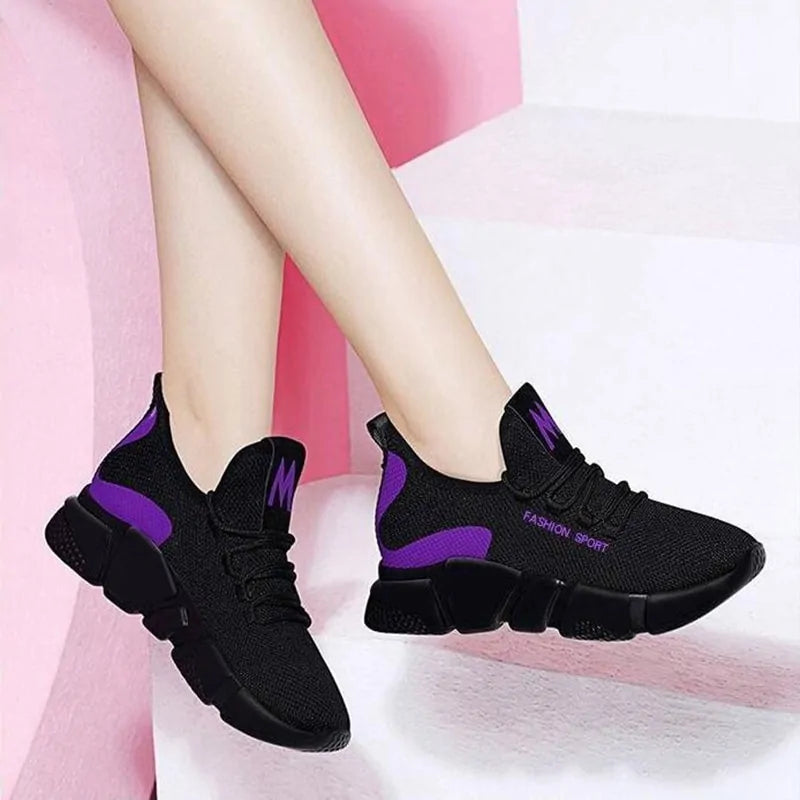 A pair of stylish black mesh sneakers worn with jeans. The shoes feature colorful embroidered details including a red and yellow daisy on the side and multicolored accents (red, blue, yellow) on the sole. The tongue displays a purple and red logo with the word "FASHION." The sneakers have a sleek, breathable design and a casual, trendy aesthetic.