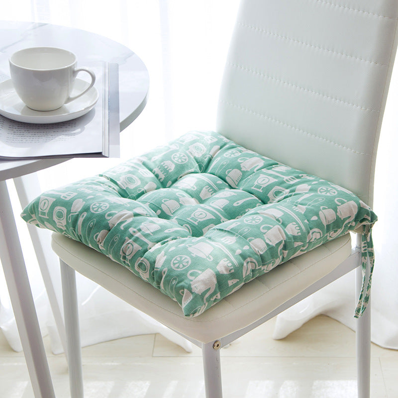 Green cushion with white patterns on a chair next to a table with a cup.