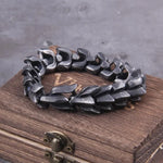 Dark metal chain-link bracelet resting on a wooden box against a gray background.