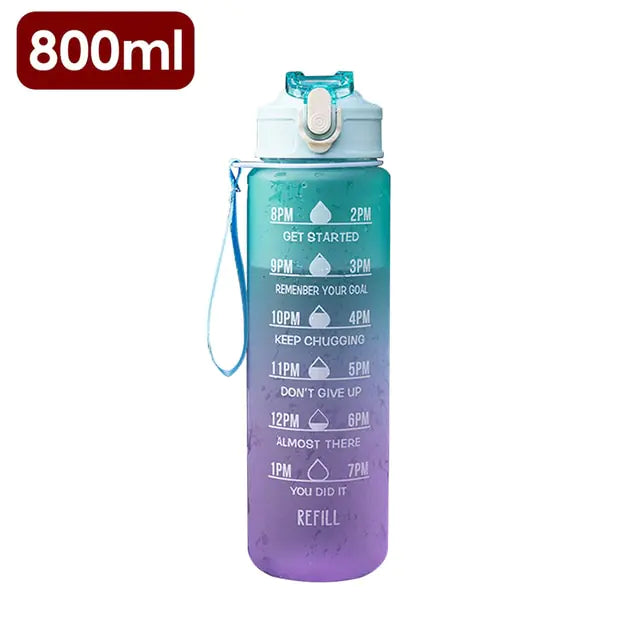 800ml gradient water bottle (teal to purple) with a flip-top lid and wrist strap, printed with hourly drink reminders from 8AM–1PM and 2PM–7PM plus motivational phrases (“Get started,” “Remember your goal,” “Keep chugging,” “Don’t give up,” “Almost there,” “You did it”) and “Refill” near the bottom.