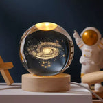 Glowing crystal ball lamp with a Milky Way galaxy design on a wooden base, sitting on a desk with an astronaut figurine in the background.