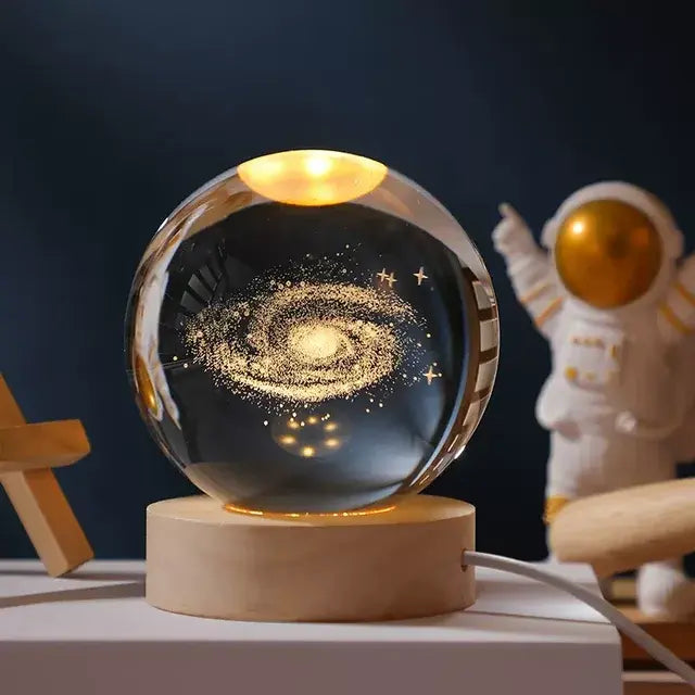 Glowing crystal ball lamp with a Milky Way galaxy design on a wooden base, sitting on a desk with an astronaut figurine in the background.