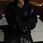 Person wearing a black hoodie and trousers embellished with rhinestone star designs, standing outdoors at night.