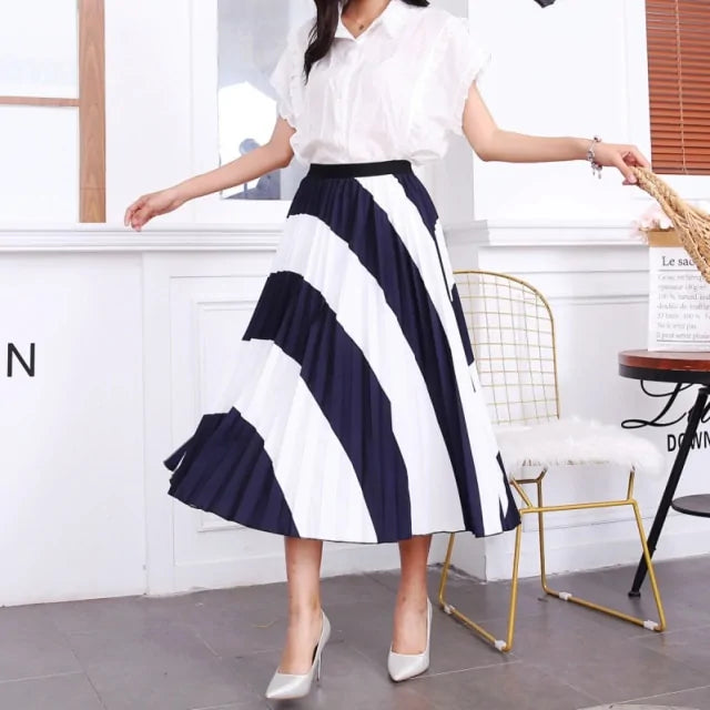 Pleated midi skirt with a gradient design, transitioning from dark black at the waistband to a soft blush pink at the hem, hanging on a black clothing rack next to a vintage-style camera.