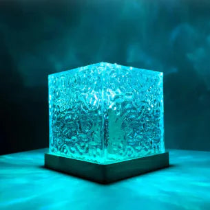 A cube-shaped decorative light with a textured glass surface, illuminated from within with a soft blue light. The cube sits on a dark base, and the lighting creates a glowing effect, enhancing the surface texture. The background features a misty, blue hue, adding to the calming ambiance of the scene.