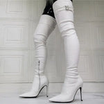 A pair of sleek, white over-the-knee stiletto boots with pointed toes and side zippers, featuring decorative buckles at the top, worn in a modern, minimalist room with textured white wall panels.