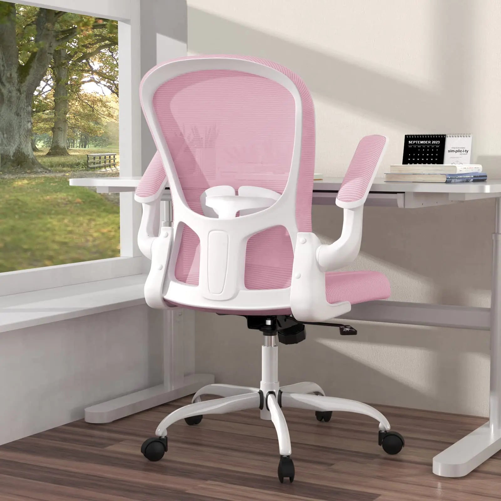Pink office chair with white frame on a desk by a window with a view of greenery.