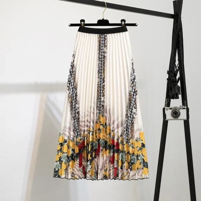 Pleated midi skirt with a gradient design, transitioning from dark black at the waistband to a soft blush pink at the hem, hanging on a black clothing rack next to a vintage-style camera.