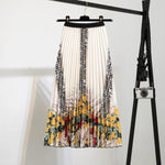 Pleated midi skirt with a gradient design, transitioning from dark black at the waistband to a soft blush pink at the hem, hanging on a black clothing rack next to a vintage-style camera.