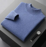 A neatly folded beige knitted sweater with a ribbed high collar and cuffs, placed on a dark grey surface. Beside the sweater, a classic wristwatch with a black leather strap and a silver dial is positioned, adding a touch of elegance to the composition.