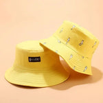 Two yellow bucket hats placed side by side against a peach-colored background. One hat has a "Goose!" label, while the other is decorated with small illustrations.