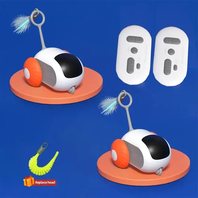 A small robotic pet toy shown on a blue background, with orange side wheels, a dangling feather teaser on top, two white remote-control pads, and a replaceable brush head accessory.