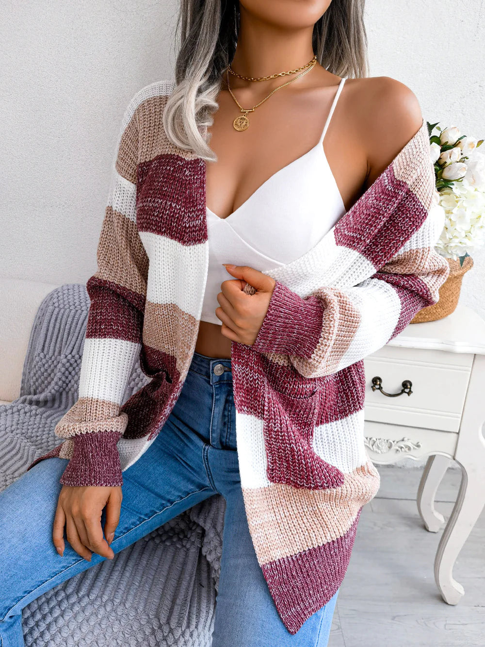 Woman wearing a striped cardigan over a white top and blue jeans, sitting on a couch.