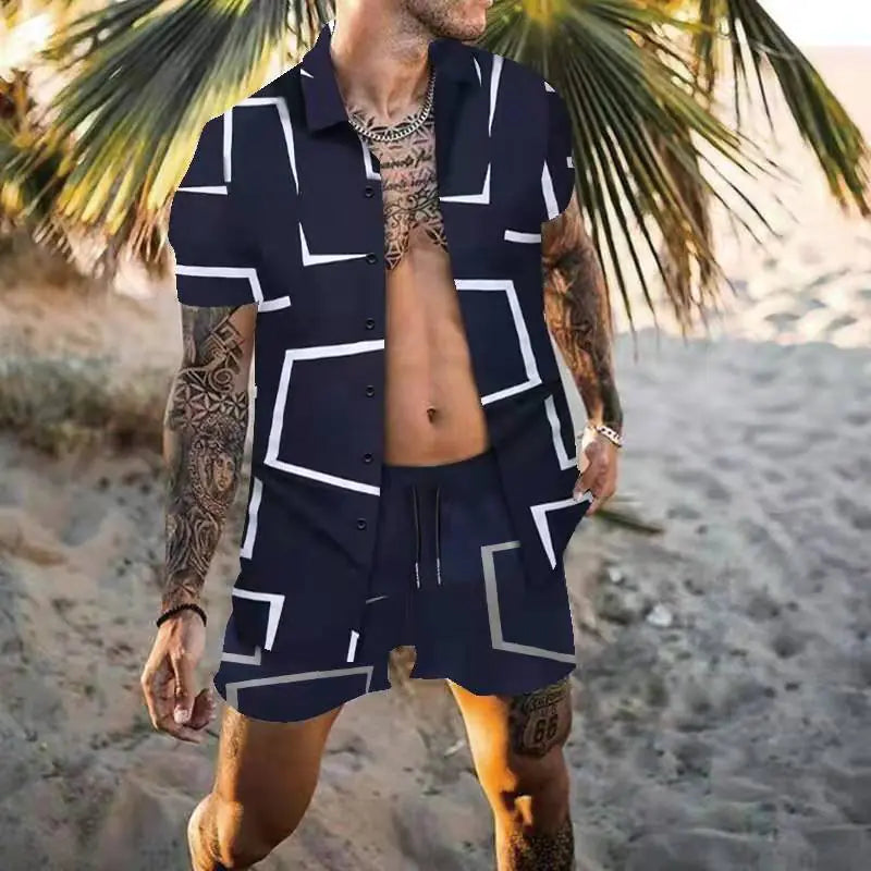 A tattooed man stands on a sandy beach wearing a stylish, matching two-piece summer outfit. The set includes a short-sleeve, button-up shirt and drawstring shorts, both in white with bold black geometric line patterns. He accessorizes with a silver chain necklace and a watch, while palm trees and beach sand provide a tropical backdrop.