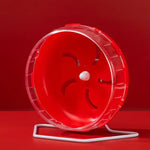 Red plastic hamster exercise wheel with a clear rim, mounted on a white metal stand against a red background.