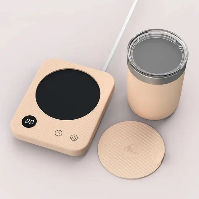 A beige electric mug warmer with a black heating plate and digital display showing “80,” placed beside a matching insulated cup with a lid and a separate round coaster, on a light surface.