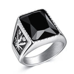 Silver signet-style ring with a large square black faceted stone on top and an engraved leaf motif on the side, shown on a white background.