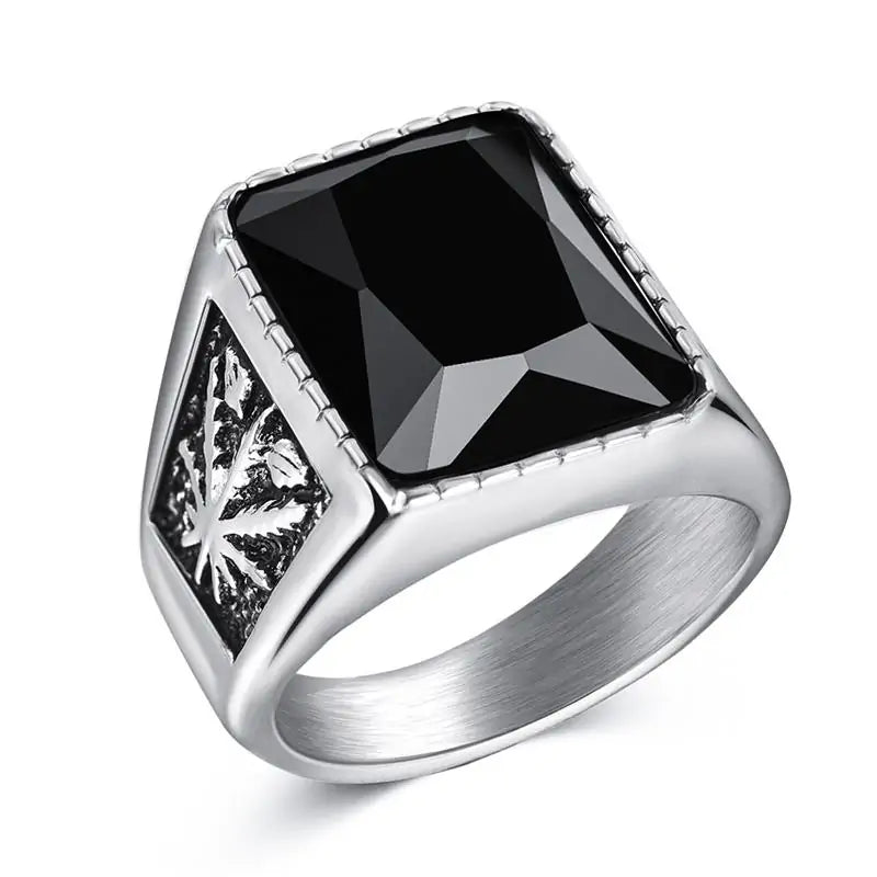 Silver signet-style ring with a large square black faceted stone on top and an engraved leaf motif on the side, shown on a white background.