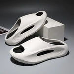 A pair of stylish black slip-on sandals with purple cushioned insoles, featuring cutout designs on the sides and toes, displayed on a white surface next to stacked books.