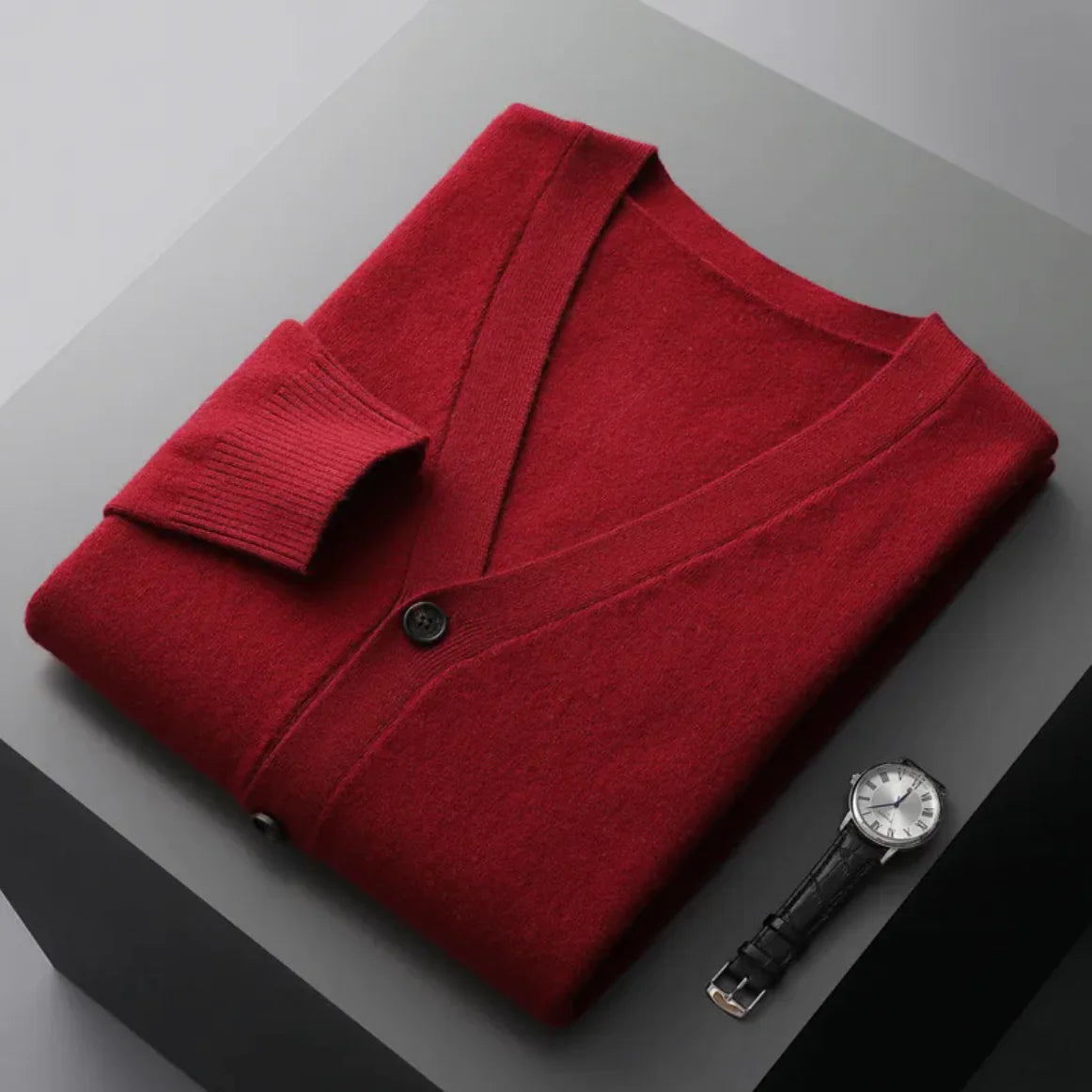 A neatly fold shirt on a black  surface with a black leather wrist-watch beside it