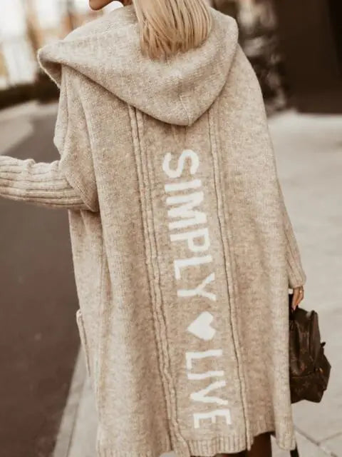 Beige hoodie with 'Simply Live' text worn by a person outdoors.