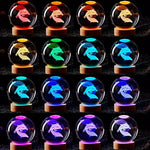 Grid of crystal ball lamps on wooden bases, each showing a 3D dragon-like figure illuminated in different colors (red, orange, yellow, green, blue, and purple) against a dark background