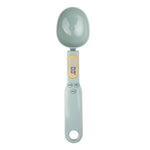 Digital kitchen measuring spoon in light gray with an oval scoop and an LCD display on the handle, shown on a white background.
