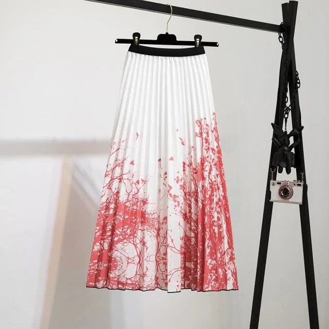 Pleated midi skirt with a gradient design, transitioning from dark black at the waistband to a soft blush pink at the hem, hanging on a black clothing rack next to a vintage-style camera.