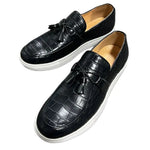 A pair of elegant burgundy leather loafers with a glossy finish. The shoes feature gold-toned metal horsebit detailing across the uppers and are displayed with wooden shoe trees inserted. They have a sleek, elongated silhouette with subtle stitching along the toe cap. The loafers are placed on a dark surface, partially framed by a wooden picture frame, emphasizing their classic and sophisticated style.