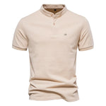A beige short-sleeved polo shirt with a mandarin collar and a two-button placket. The fabric appears soft, and there is a small embroidered logo on the left chest. The shirt has a modern, slim fit with neatly stitched hems.