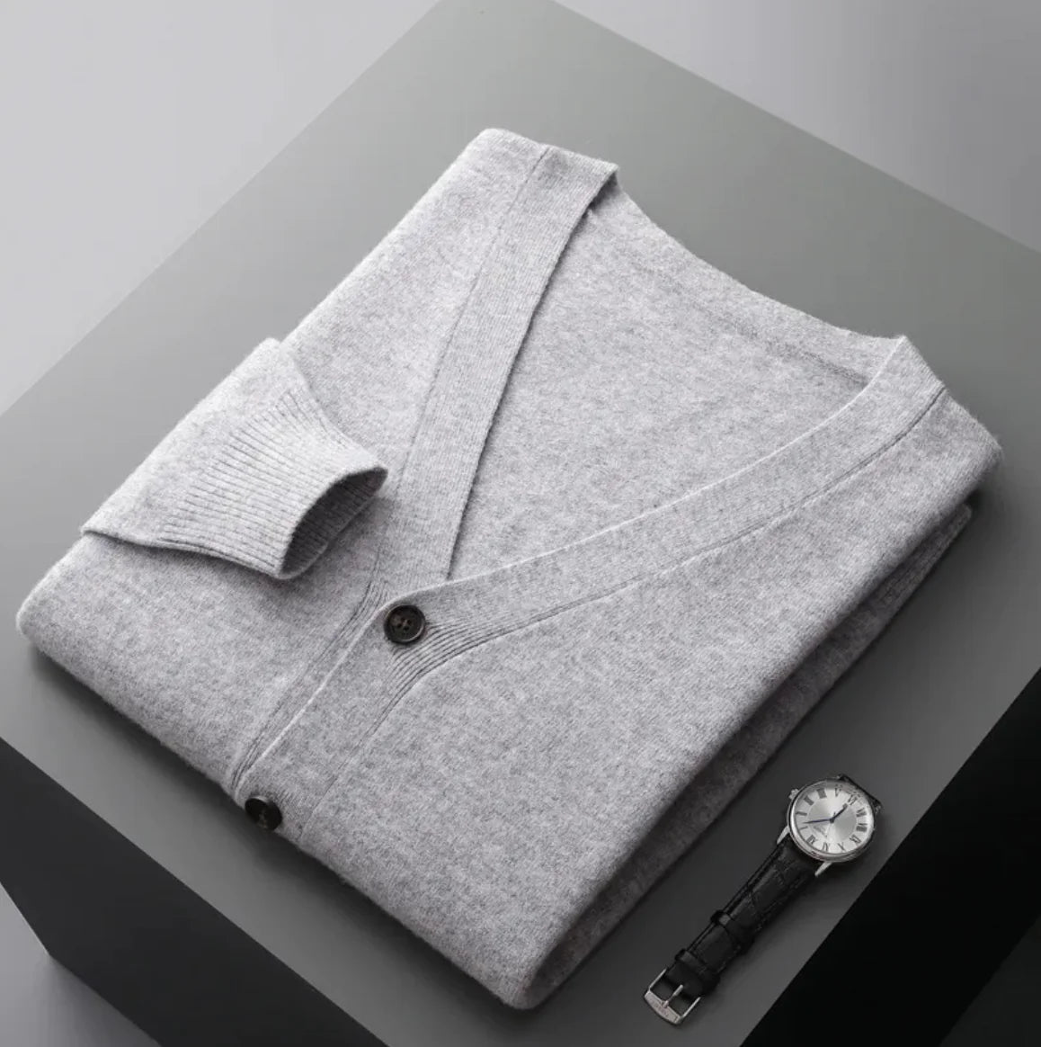 A neatly fold shirt on a black surface with a black wrist watch near it