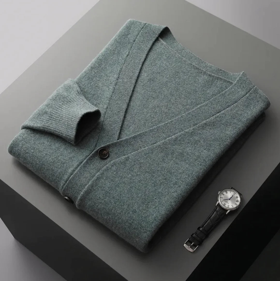 A neatly fold shirt on a black box with a black leather watch beside it