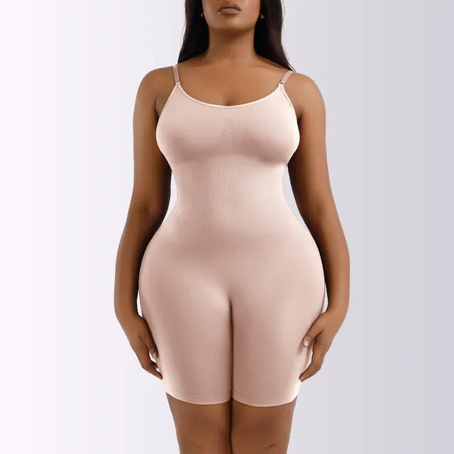 A nude beige full-body shapewear bodysuit shown on a model, featuring thin adjustable straps, a scoop neckline, and mid-thigh shorts. The seamless design is form-fitting and made to smooth and contour the waist, hips, and thighs for a streamlined silhouette under clothing.