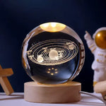 A glowing crystal ball lamp with a golden spiral galaxy design inside sits on a wooden base, softly illuminated, with a small astronaut figurine standing in the background against a dark backdrop.