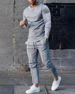 Man walking outdoors wearing a light gray long-sleeve fitted shirt and matching slim jogger-style pants with seam details, paired with white sneakers.