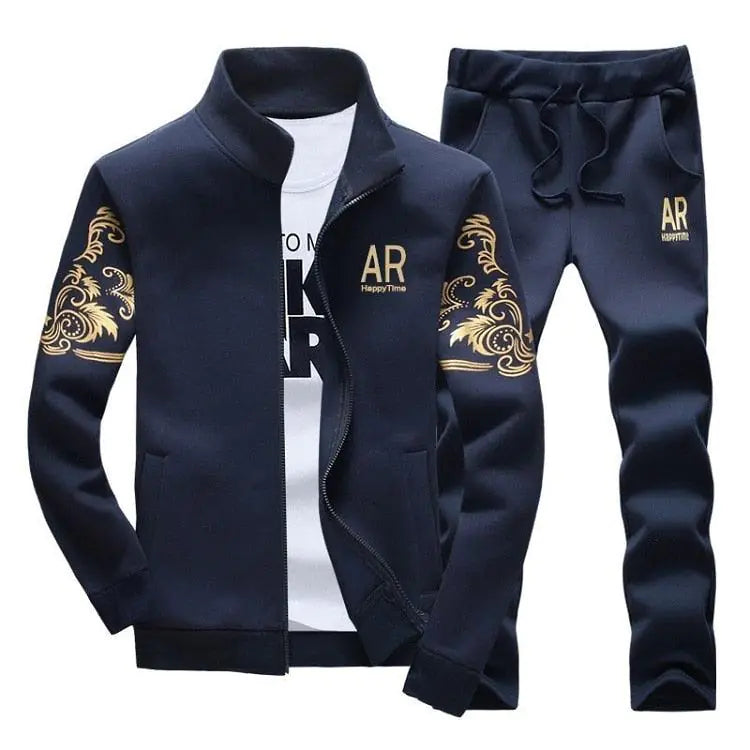 A navy blue men’s tracksuit set: zip-up stand-collar jacket and matching jogger pants, both with gold decorative swirl prints and an “AR” logo; shown on a white background with a white T-shirt underneath the jacket.