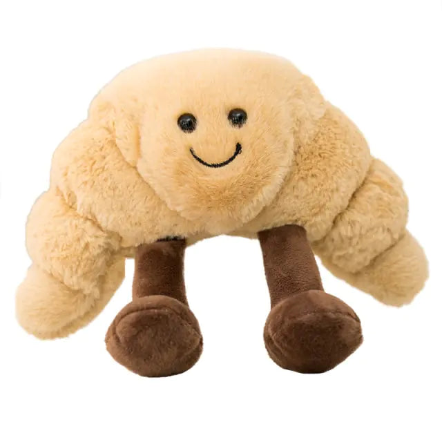 Cute plush croissant toy with a stitched smiling face and four dangling brown legs, on a white background.